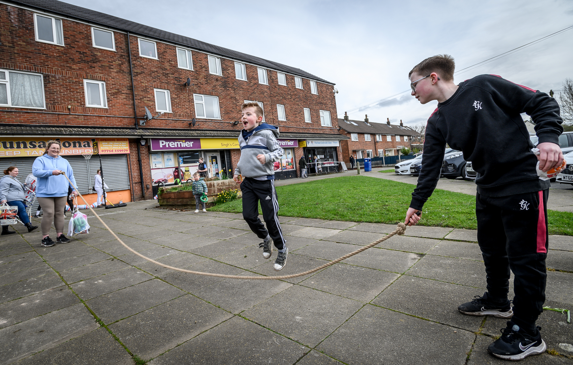 A young boy skipping with a long rope held by a woman and a teenage boy at The Base fun day.