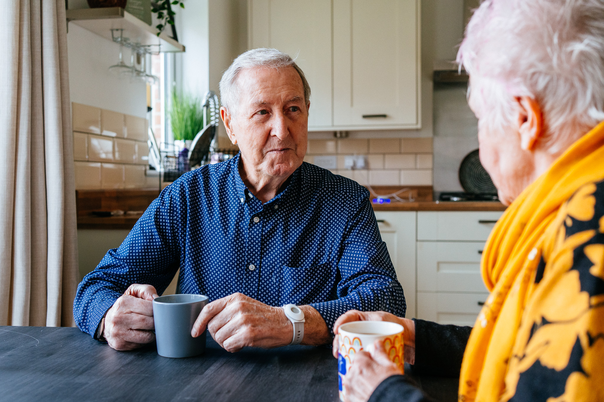Couple enjoying a cup of tea together in their kitchen, smiling and relaxed.