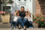 Lady with her 2 children smiling sitting at their front door in the sunshine 