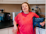 Lady in kitchen holding a blue handbag, smiling